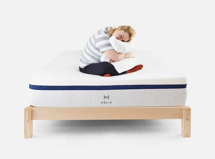 woman sitting on helix mattress on helix natural wood bed frame