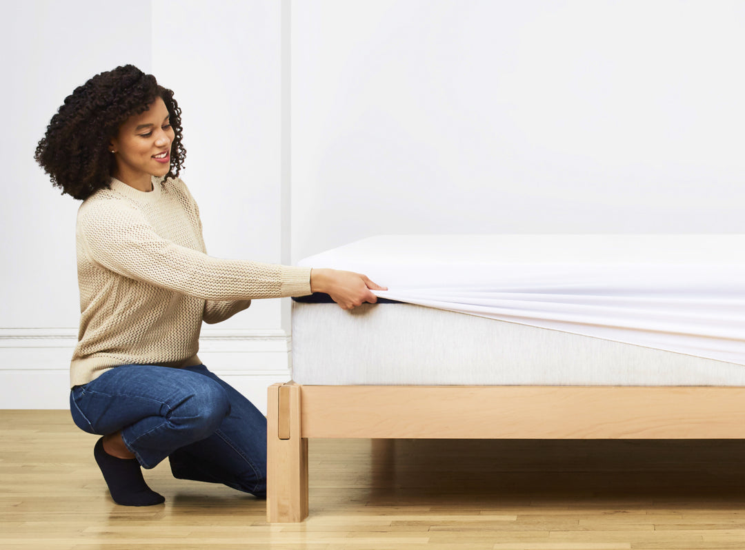 An image of the Waterproof Mattress Protector with a woman pulling the protector across the surface of a mattress